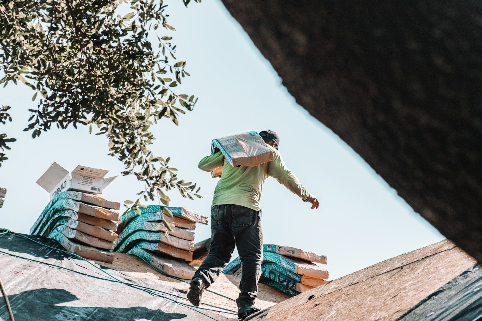 A person carrying a bundle of shingles across a residential roof