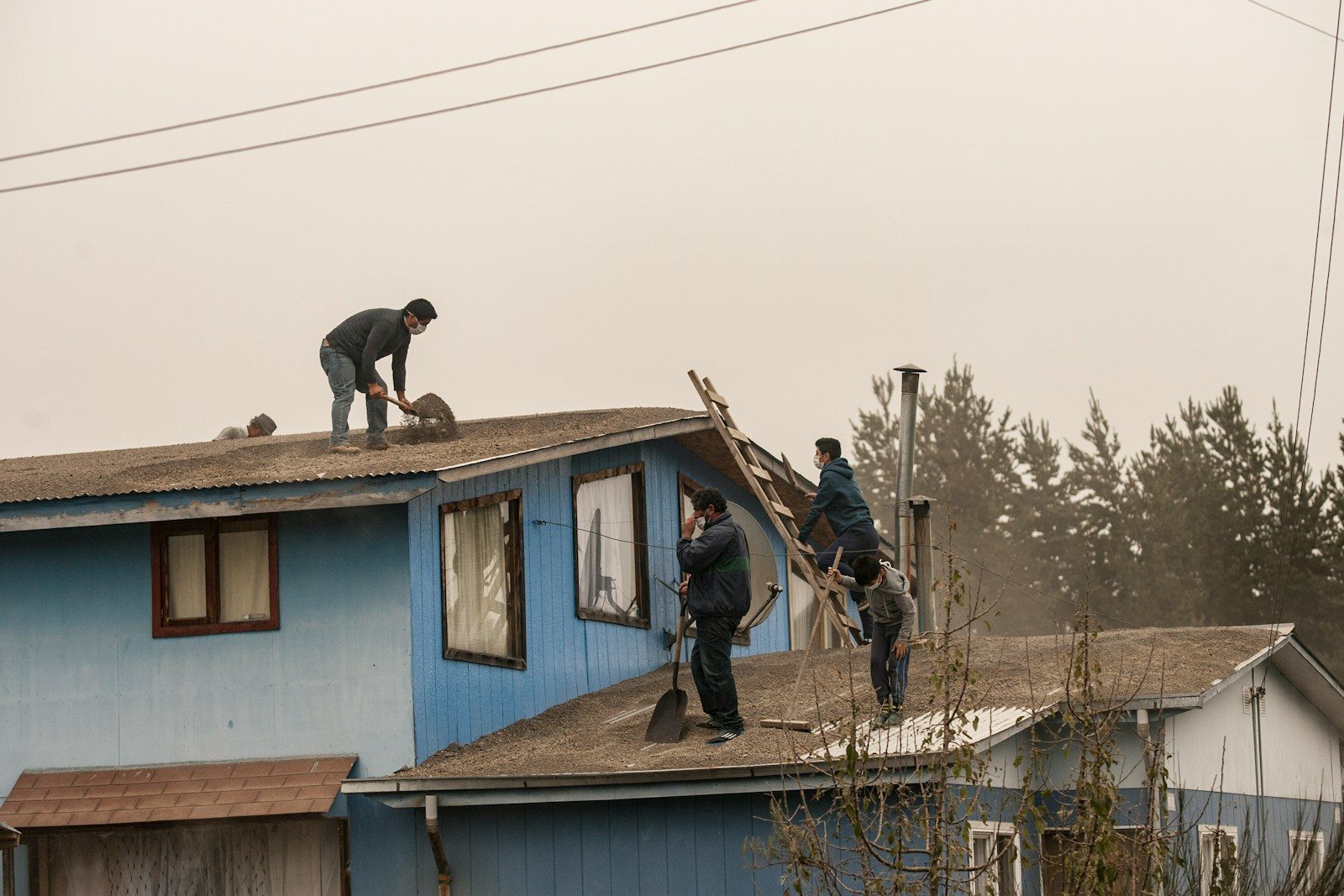 Men cleaning ash from blue house roofs
