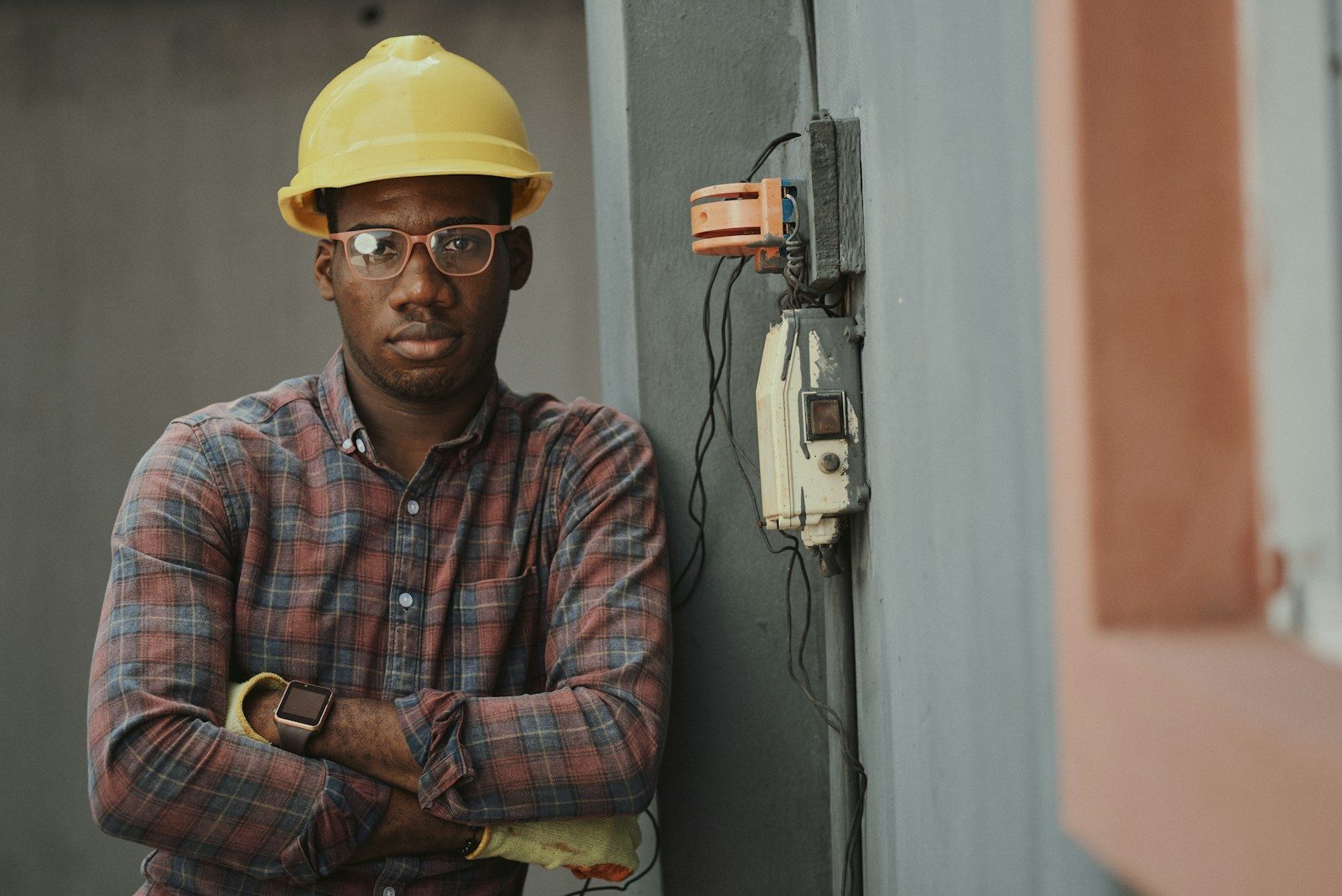 A person in a yellow hard hat and plaid shirt leaning against a wall