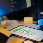 Cluttered desk with tablet showing a green checked to-do list, sticky notes, a calculator, and a hand holding a white card.